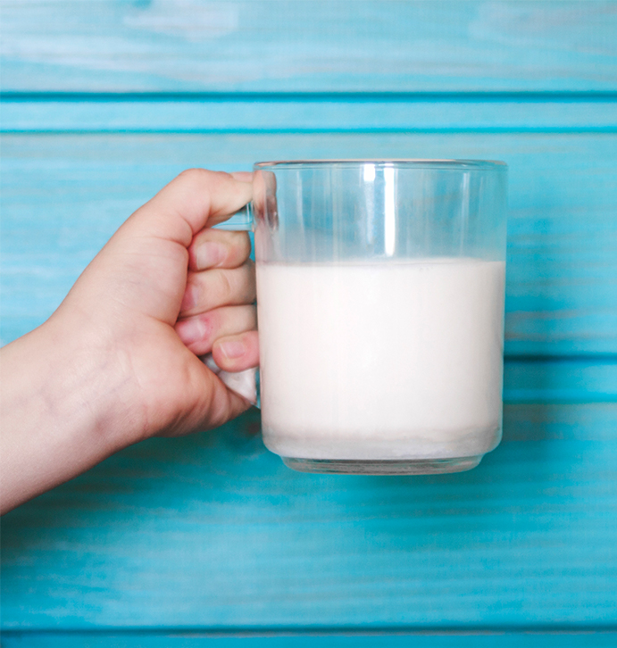 Milk-691x426 Woman’s hand with a glass of fresh milk at a party against a blue wooden wall