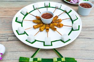 A white plate with sticks of chicken satay and lontong cubes arranged to form the shape of the Singapore Flyer