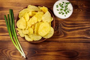 Top view of crispy potato chips with green onion and sour cream on wooden table