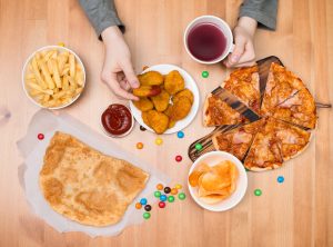 Top view of hand holding a chicken nugget with other fast food on a wooden table Top view of hand holding a chicken nugget with other fast food on a wooden table