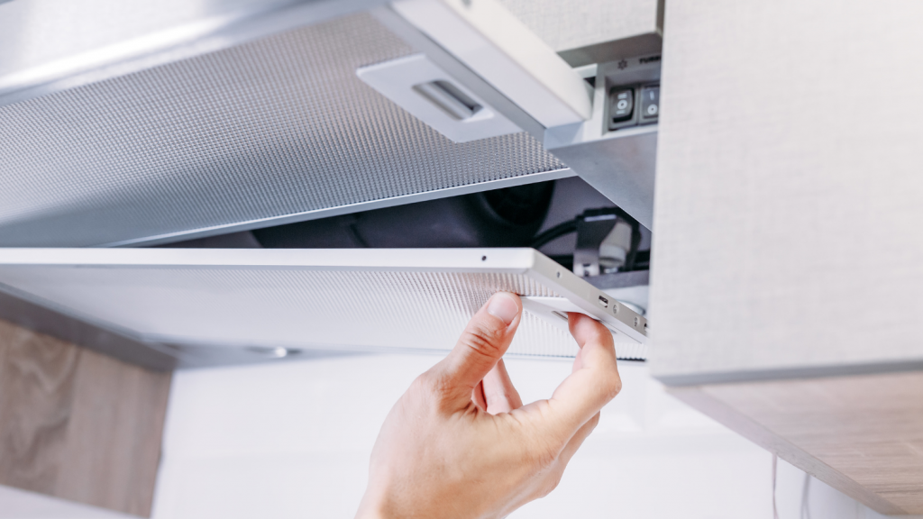 Cleaning the lid underneath a silver kitchen hood