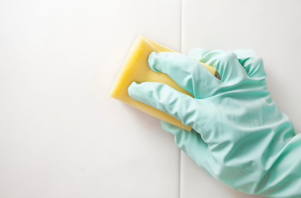 Pastel green glove and yellow sponge cleaning white tiles