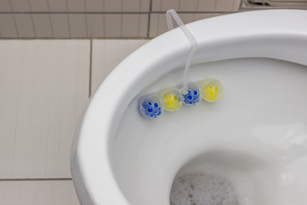 Blue and yellow cleaning balls attached to a toilet bowl rim