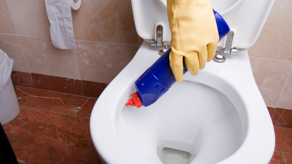 Blue bottle of gel being squirted on the inside of a white toilet bowl rim