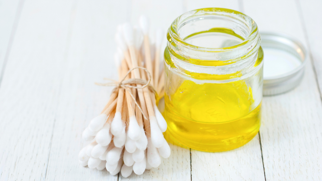 Baby oil in a jar and cotton buds on a white wooden table