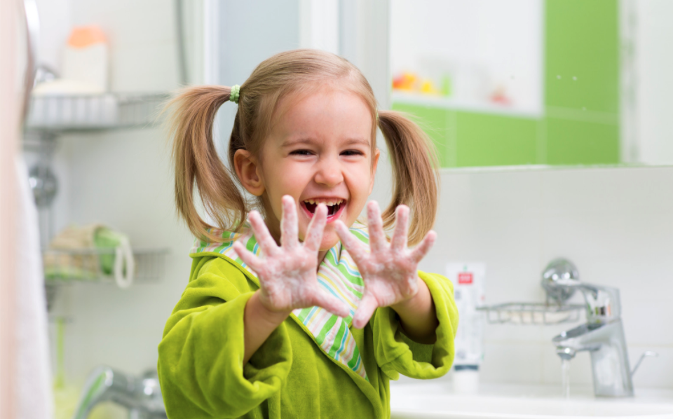 Young Caucasian girl in a green jacket holding up her washed hands