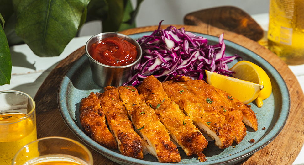 Crispy fried chicken schnitzel served with a side of salad and curry ketchap