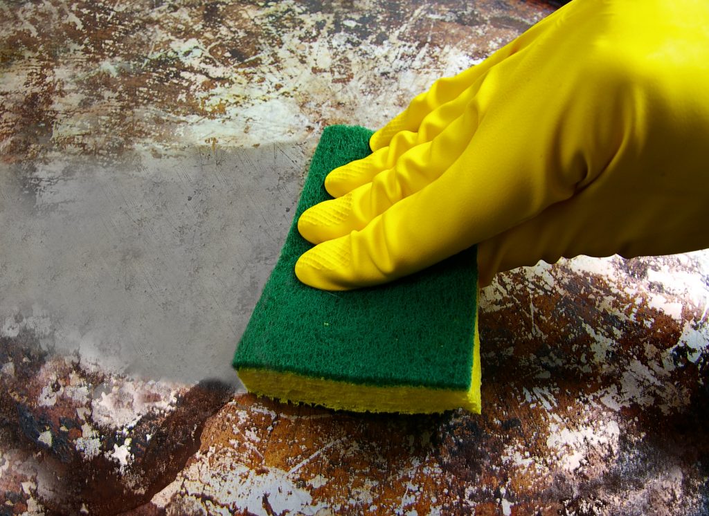 Gloved yellow hand scrubbing a dirty metal surface