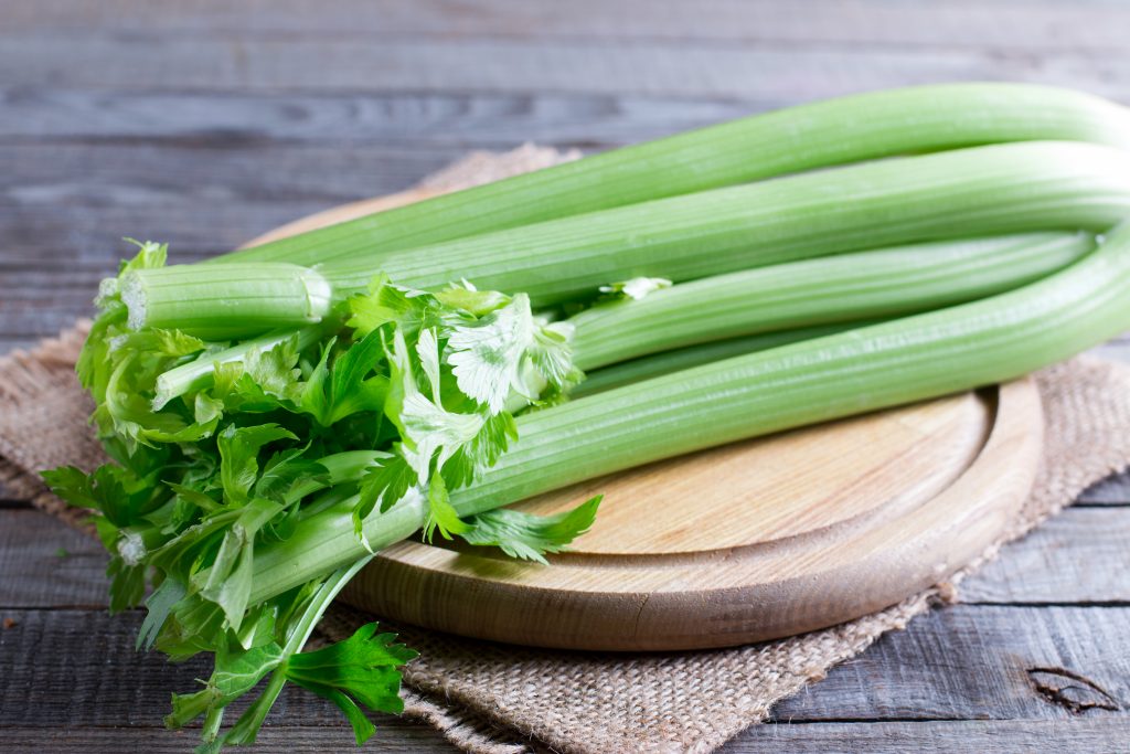 Fresh green celery stems on wooden cutting board