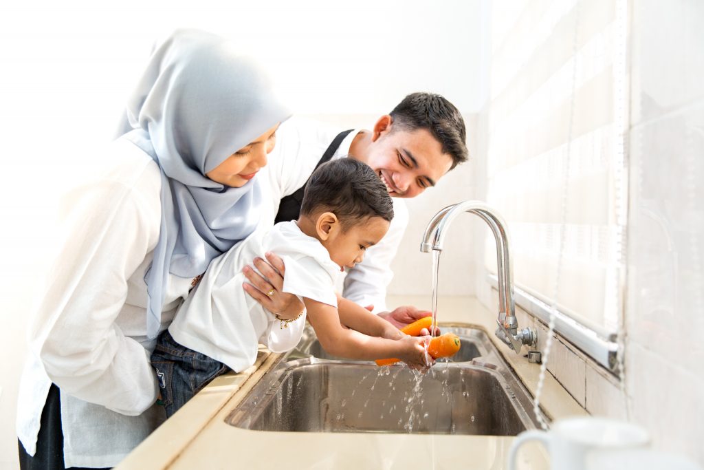 Cute child washing carrot while hugged by mother from behind