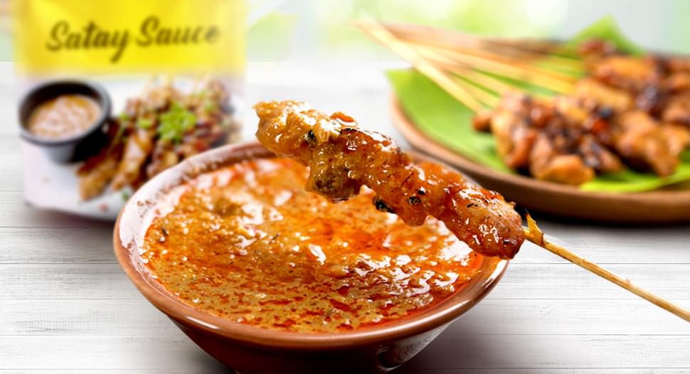 Satay hovering above a bowl of peanut dipping sauce Satay