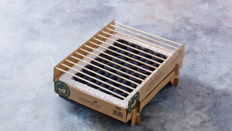 The Casus Grill A portable barbecue grill made with cardboard and bamboo sticks, set against a marbled grey background