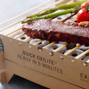 Casus Grill closeup with food A thin slab of steak, two sticks of asparagus and tomatoes on the vine being cooked on a portable BBQ grill made of cardboard and bamboo