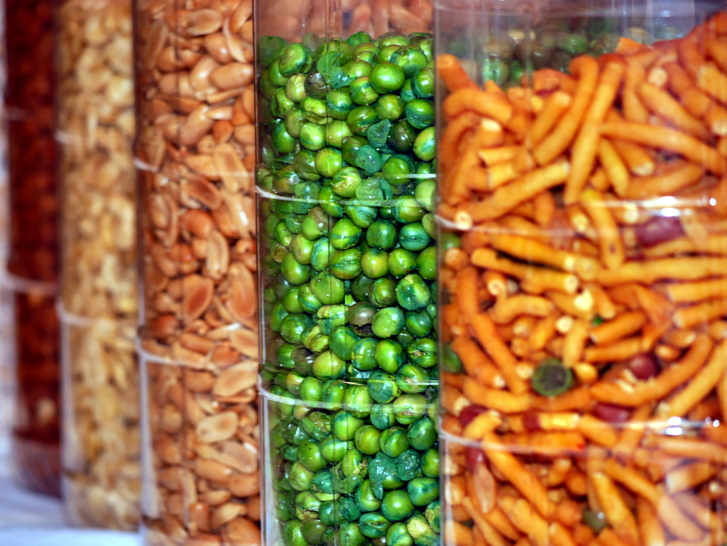 Kacang Puteh A row of large transparent containers, each filled with peanuts, dried green peas and other assorted kacang puteh nuts