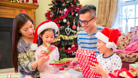 Asian parents and two kids opening up presents in the living room at Christmas