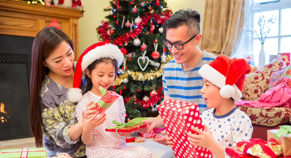 Asian parents and two kids opening up presents in the living room at Christmas