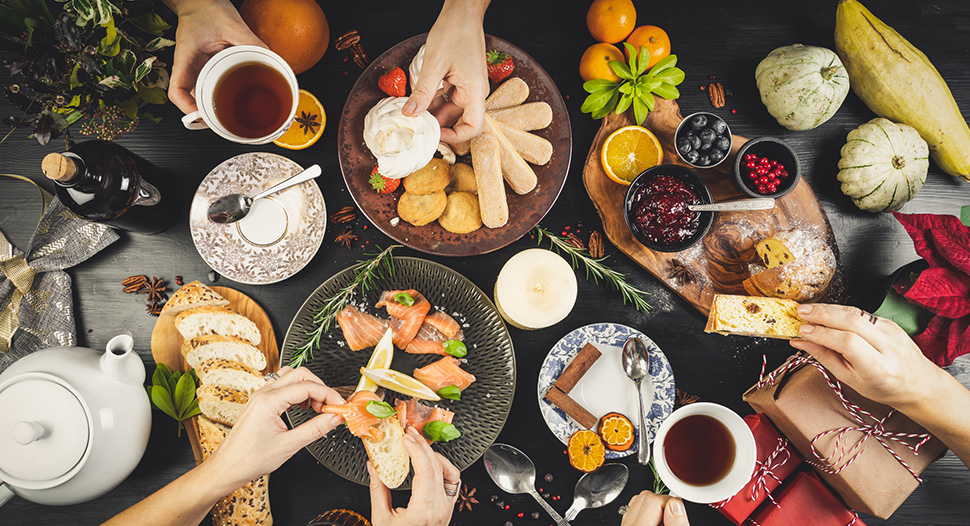 Top view of a table laden with food for Christmas, and hands sharing food over the table