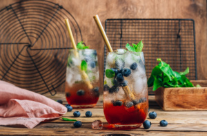 Blueberry ice mojito with mint in tall glasses on rustic wooden background.